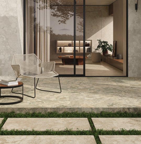 Outdoor area with woven seating and coffee table on stone-effect stoneware flooring, view of the living room with large sliding glass doors.
