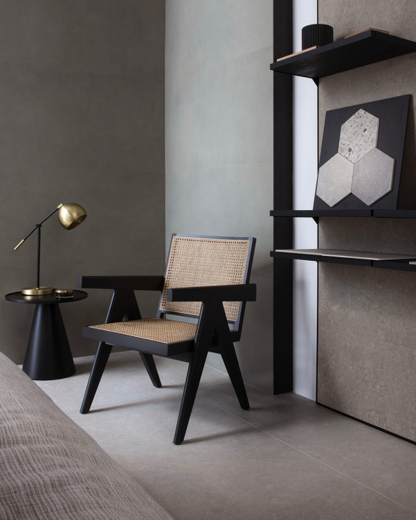 Elegant reading corner with grey stoneware wall, modernist wooden and straw chair, black coffee table and satin brass wall lights.
