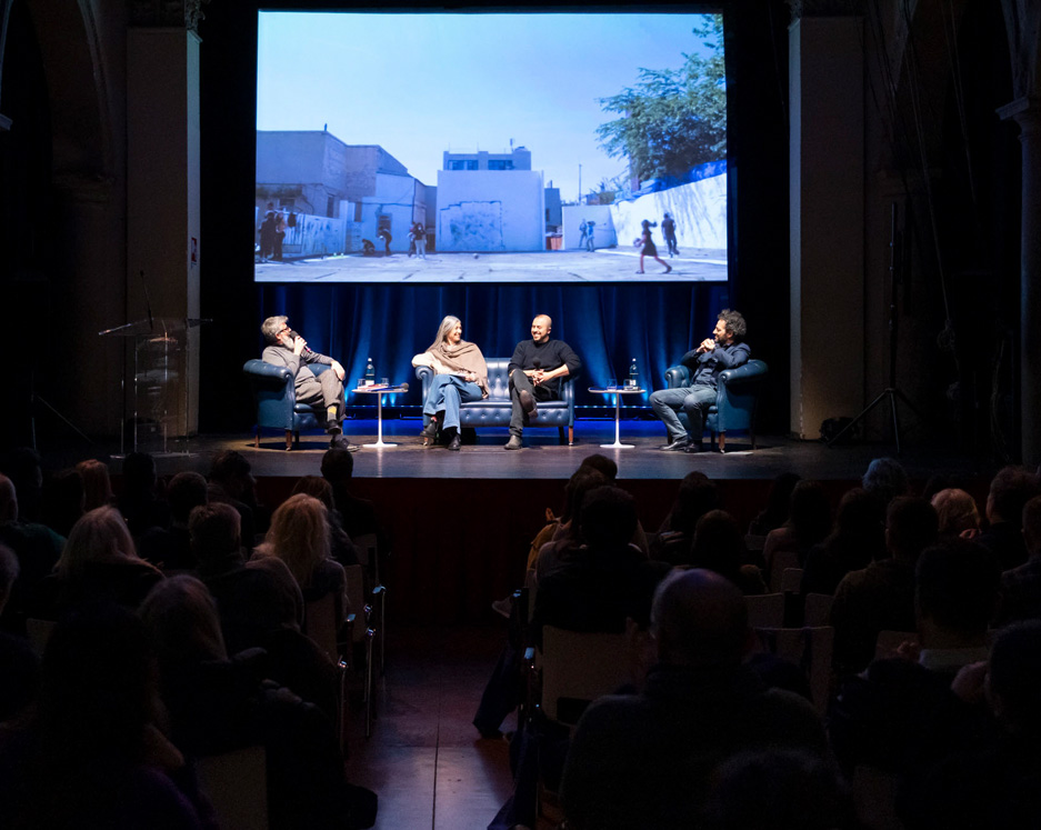 Urban art event with artists and speakers on stage and photos of murals projected onto the theatre backdrop.