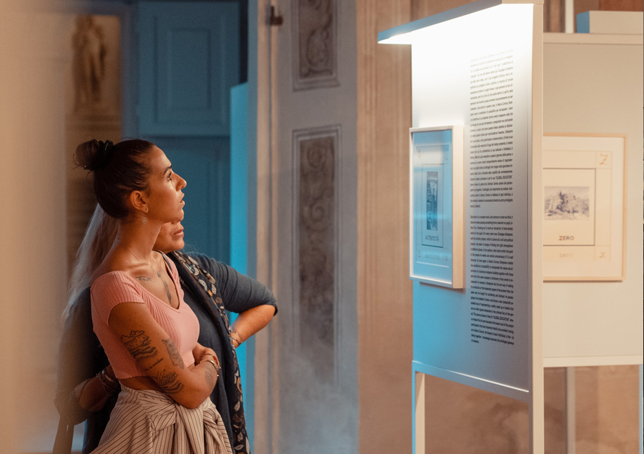 Two women observe an illuminated display panel during a cultural exhibition hosted in a historic space.