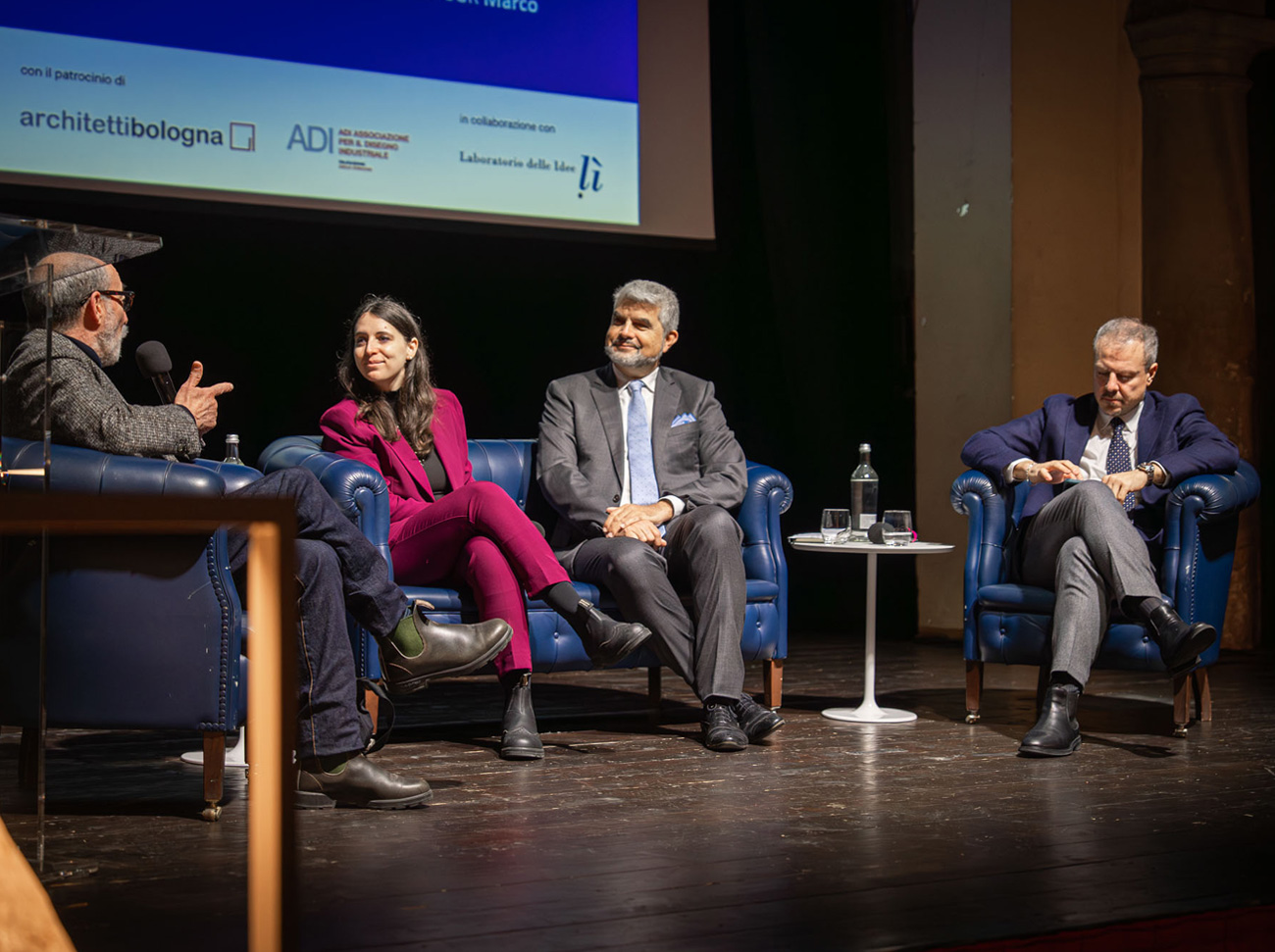 Tavola rotonda con quattro relatori seduti su poltrone blu sul palco.
