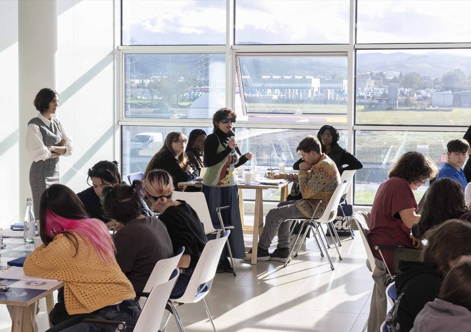 Educational activity with students in a glass-walled classroom, with moments of discussion, active participation and a view of the industrial landscape outside.