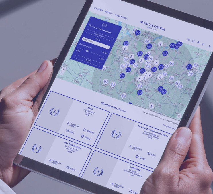 Hands holding a tablet with an interactive map of the Marca Corona site, active retailer search function and visible results.