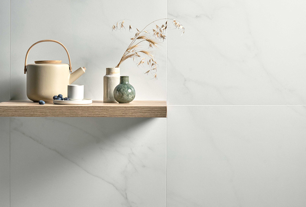 Holzregal mit cremefarbener Teekanne und Keramikvasen an einer Wand aus weißem Marmor-Effekt-Steingut aus der Kollektion Scultorea Delicata.