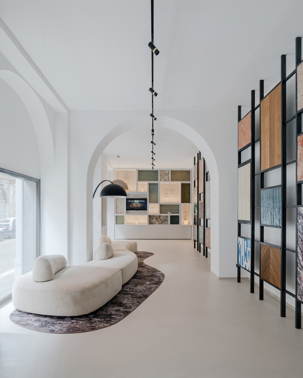Showroom with Marca Corona material display, minimalist curved furniture, white arched walls and continuous resin-effect flooring.