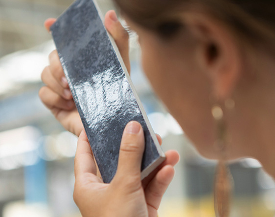 Close-up of a woman carefully examining a glazed tile, symbolising the care, aesthetic research and product quality of Italian porcelain tile manufacturers.