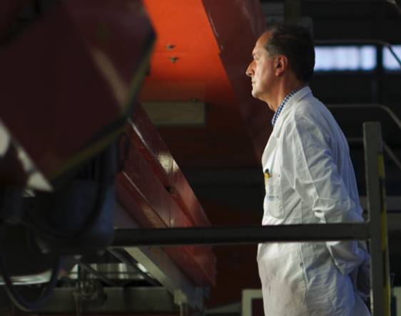 A technician in a white coat observes industrial machinery in a factory, a symbol of research and quality control.