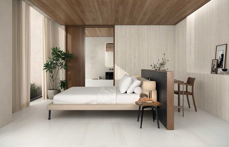 Hotelzimmer mit Bodenbelag und Wänden in weißer Travertinoptik, Holzdecke und Möbeln in neutralen Farbtönen mit essentiellem Design.
