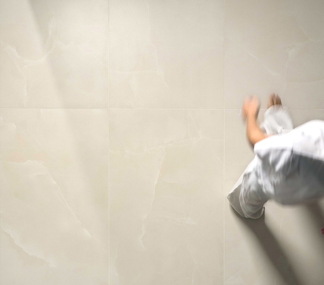 Bodenbelag aus Feinsteinzeug in cremefarbener Marmoroptik mit glänzender Oberfläche, durchflutet von natürlichem Licht und bewegten Figuren.