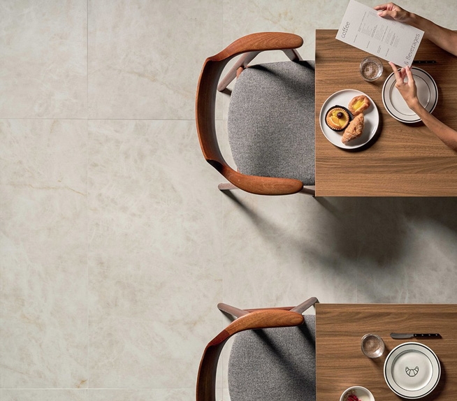 Objektbereich mit hellem Bodenbelag in Marmoroptik und Einrichtung aus Holz und grauem Stoff, beleuchtet durch Tageslicht.