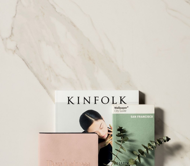 Detailansicht einer hellen Marmoroptik mit goldenen Adern, kombiniert mit Zeitschriften und minimalistischen Dekoartikeln.