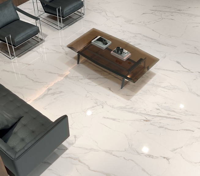 Wohnbereich mit Bodenbelag in weißer Marmoroptik mit grauen Adern, modernen Möbeln aus Leder und Metall und einem Tisch aus Rauchglas.