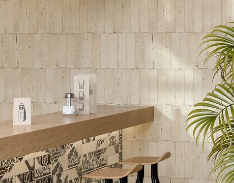 Dettaglio bancone bar con piano legno, rivestito in gres effetto maiolica nero su fondo beige, pareti rivestite piastrelle ceramiche beige, sgabelli legno-metallo.
