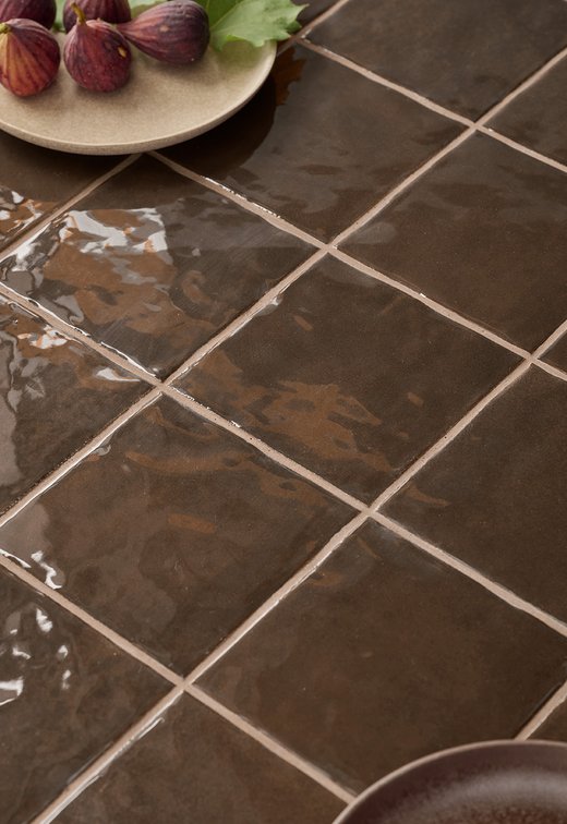 Bagno moderno con piastrelle corten effetto bruciato e beige chiaro, vasca integrata e dettagli decorativi naturali e dorati.