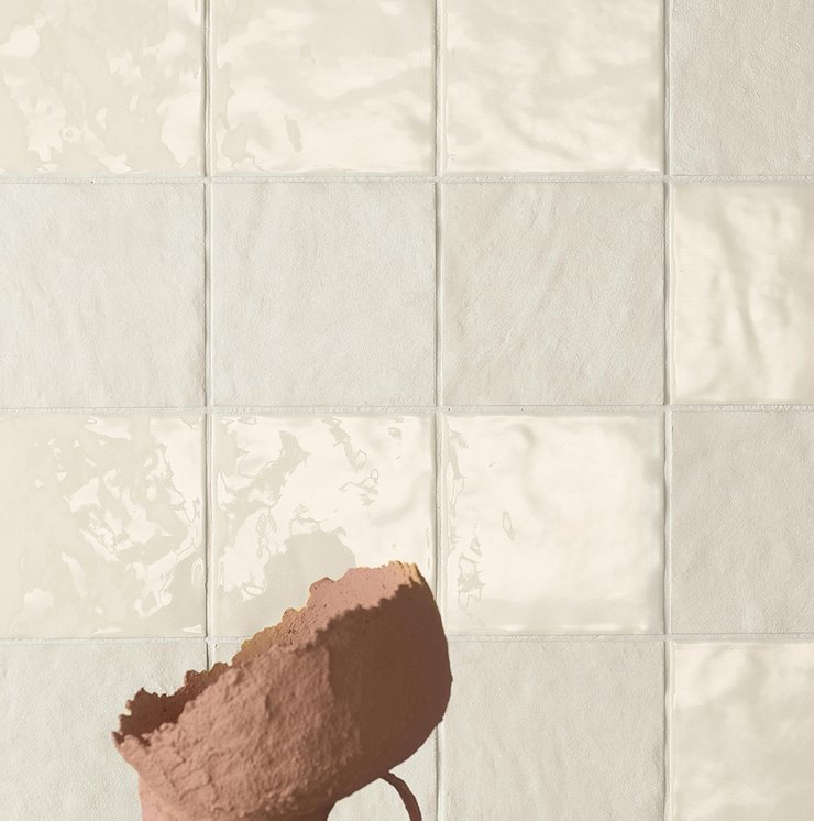 Dettaglio camino con rivestimento ceramico verde rame e parete terracotta, legna e fuoco acceso.