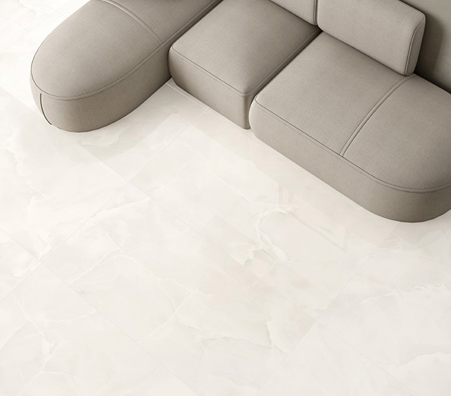 Bodenbelag aus Feinsteinzeug in weißer Marmoroptik mit perlmuttfarbenen Adern und beiges Sofa mit weichen Linien in einem hellen Wohnzimmer.