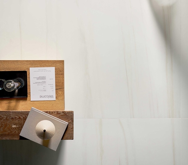 Bodenbelag aus Feinsteinzeug in weißer Marmoroptik mit zarter beiger Maserung, Ablagefläche aus Holz mit Dekorationsgegenständen.