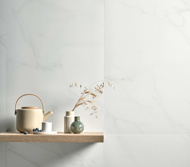 Wandverkleidung aus Feinsteinzeug in weißer Marmoroptik mit leichter Maserung, Regal aus hellem Holz und Keramikdekorationen.