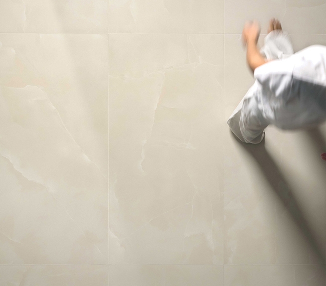 Blick von oben auf eine unscharfe Person, die auf einem cremefarbenen Feinsteinzeugboden mit Marmoreffekt und glänzender Oberfläche läuft.