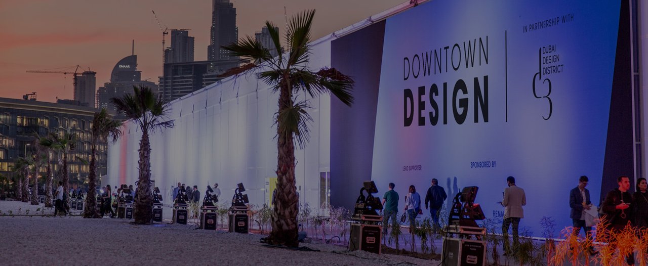 Vista exterior nocturna de un evento de diseño con pabellón iluminado y horizonte urbano.