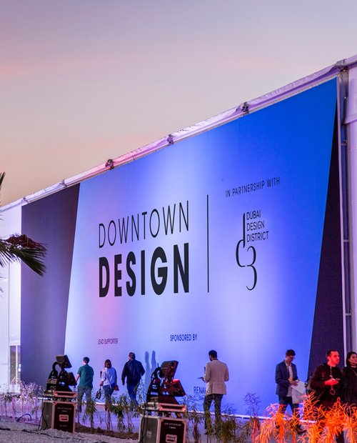 Vista exterior nocturna de un evento de diseño con pabellón iluminado y horizonte urbano.