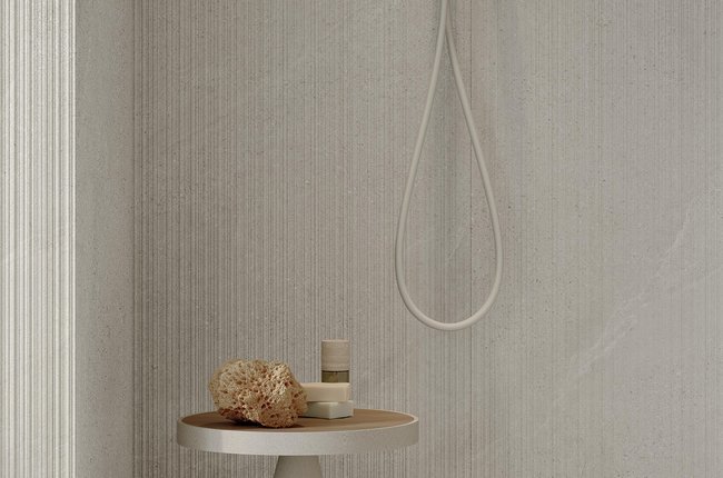 Minimal shower with beige stone‑effect porcelain tiles and round side table.