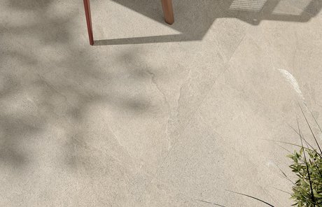 Detail of outdoor stone‑effect porcelain flooring with plant shadows.